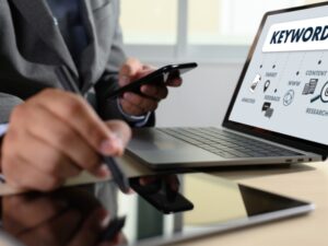 Businessman using a smartphone and laptop with a keyword analysis chart, highlighting the importance of a schema markup generator.